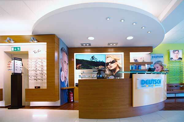 Modernes Optikergeschäft mit Empfangstheke, Brillenauswahl und Werbeplakaten.